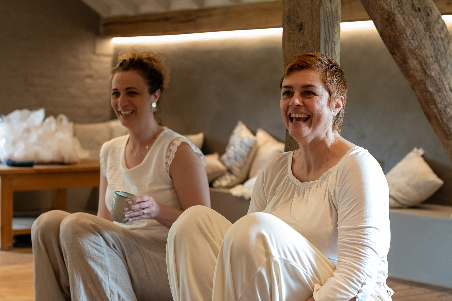 Twee vrouwen lachen samen tijdens een pauze in een warme, houten ruimte